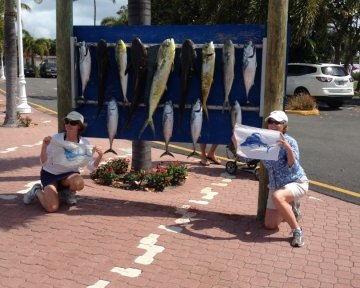 Two women holding up blue marlin flags in front of the sailfish marina sign